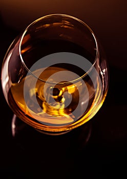 Top of view of snifter of brandy in elegant typical cognac glass on dark background with golden reflection