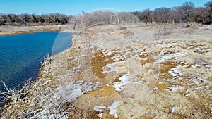 Top view snow covered rocky shoreline with dry tree stumps along crystal water of Lake Grapevine, Texas, USA