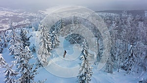 Top view of snowboarder riding downhill in forest at ski resort, aerial shot