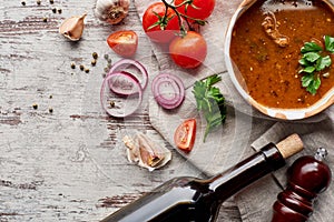 Top view of soup kharcho, wine bottle, vegetables and spices on table.