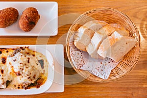 Top view of Spanish fresh baked bread in basket with Lasagne and Papas Rellenas. Served as appetizer photo
