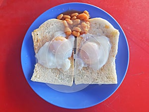 Top view a special breakfast of toast with half-put eggs and red beans on red background