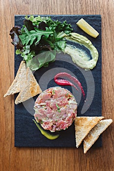 Top view of Spicy Bluefin Tuna Tartare with sour and spicy sauce. Served with toast and salad on black stone plate