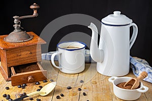 Top view of spoon, cloth, brown sugar, cup with coffee, coffee pot and old grinder on wooden table and black background