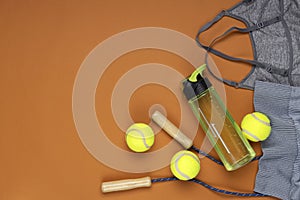 Top view of sport clothes,green balls,jump rope and bottle of water on the dark orange background.Empty space