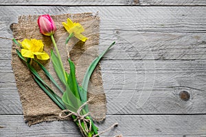 Top view of spring flowers bouquet. Yellow daffodils and pink tulip on wooden background. Copy space