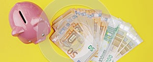 Top view of stack of euro bills and piggy bank on yellow background