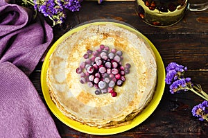 Top view on a stack of thin pancakes with cranberries, on a wooden table for a holiday Shrovetide.