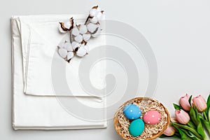 Top view of a stack of white bedsheets sets, cotton branch and a basket with Easter eggs. Copy space