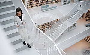 Top view, stairs and woman in library, tablet or online research for university, reading or education. Female, girl or