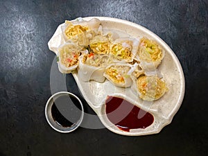 Top view of steamed vegetable and shrimp springrolls on a plate, on textured black table in restaurant. Dish is accompanied by