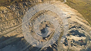 Top view of stepped quarry. Shot. Quarry with working dump trucks and excavators. Open pit works in morning. Mining