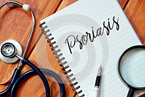 Top view of stethoscope,magnifying glass,pen and notebook written with Psoriasis on wooden background. Health concept.