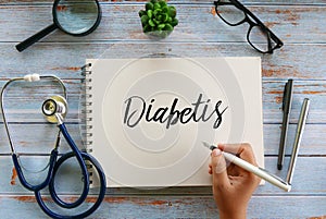 Top view of stethoscope,magnifying glass,plant,glasses,pen and hand writing ` Diabetis ` on notebook on wooden background photo