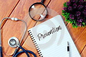 Top view of stethoscope,magnifying glass,plant,pen and notebook written with Prevention on wooden background. Health concept. photo
