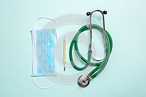Top view of stethoscope, mercury thermometer and a protective face mask on colorful background. Medical equipment and health care