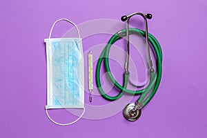 Top view of stethoscope, mercury thermometer and a protective face mask on colorful background. Medical equipment and health care