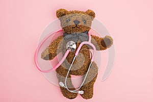 Top view of stethoscope on teddy bear on pink background, international childhood cancer day concept. photo