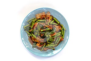 Top view of Stir fried pork belly and red curry paste with string bean in blue plate on white background.