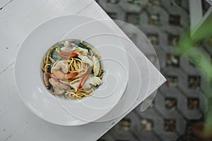 Top view of Stir-fried Spicy Spaghetti Seafood or `Spaghetti Pad Kee Mao`, fusion food in Thai Style serve with white dish.