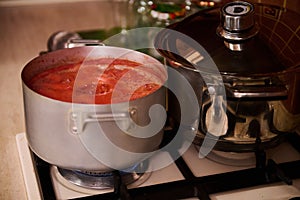 Top view of stirring boiling tomato juice, preparing homemade passata from ripe organic juicy tomatoes in the saucepan