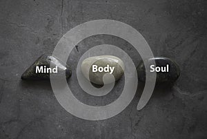 Top view of a stone written with Mind Body Soul on grey background