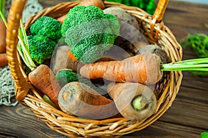 Top view Straw Basket with garden Vegetables - fresh carrots, beets, broccoli, onions on the rustic wooden background. Farm Harves