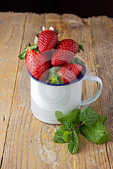 Top view of strawberries in white cup with mint leaves on rustic wooden table