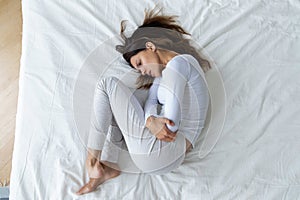 Top view stressed unhappy young woman lying in fetal position