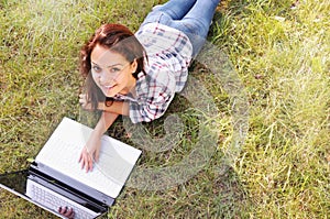 Top view of student girl working on laptop, lying on grass in park