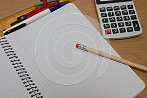 Top view of a student table with an open notebook, a pencil, a calculator, a compass and a ruler