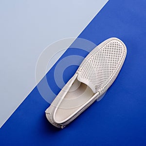 Top view of stylish ivory perforated leather men\'s moccasin shoe isolated on a creative two-tone blue background