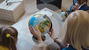 Top view. A stylish teacher with a tattoo shows the kids a globe. Teacher discussing over a globe with kids in geography