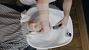 Top view. Stylist washes the hair of the young guy in the beauty salon or barbershop. Barber washing hair of his little