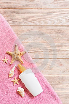 Top view of summer beach staff with copy space. Seashells or seastar, a bottle of suncream and pink towel on wooden background.