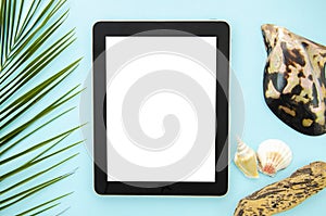 Top view summer internet surfing mockup. Tablet pc on a blue background with palm leaf and seashell. White copy space