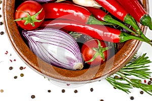 Top view of summer vegetables: onion, garlic, tomato, red chili pepper, rosemary in brown wooden bowl and peppercorns on white