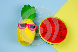 summer vibrant blue and yellow background with funny pineapple toy in sunglasses and squishy toy watermelon