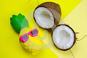 summer vibrant yellow background with funny pineapple toy in sunglasses and coconut