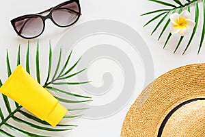 Top view of suncream, straw hat, palm leaf, sunglasses. spf cream on white background with copy space. Directly above. Bright
