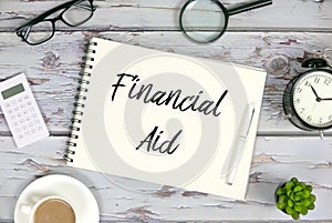 Top view of sunglasses,magnifying glass,clock,plant,coffee,calculator,pen and notebook written with Financial Aid