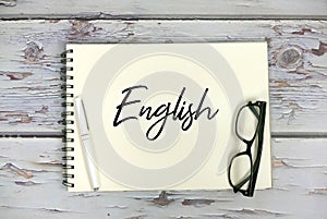 Top view of sunglasses,pen and notebook written with English on wooden background