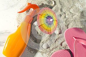 Top view of sunscreen,flip flop,little beach umbrella on sandy shore.Warm colors