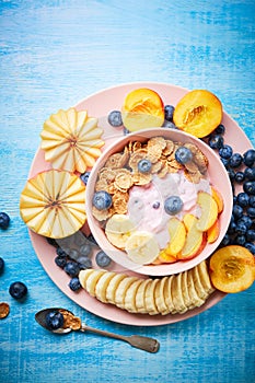 Healthy breakfast bowl berry greek yoghurt with frefh blueberries, banana and flakes on the blue wooden table