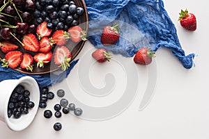 Top view of sweet blueberries on bowl, cherries and cut strawberries on plate with blue cloth.