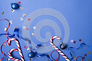 Top view of sweet candy canes, christmas bulbs, confetti and dcorative ribbons on the blue background