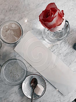 A top view table with a blank menu and drinks in a Cafe, cappuccino and orange juice, sweets and a pink rose