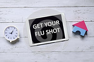 Top view of table clock and tablet written with Get Your Flu Shot on wooden background.