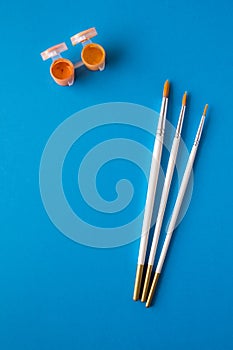 Top view of the table. Set of different artist brushes and multi-colored paint for drawing in small banks on a blue background