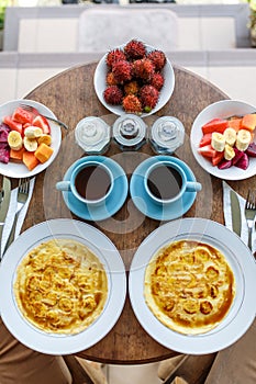 Top view, table setting. Balinese tropical breakfast of fruit, coffee and scrambled eggs and banana pancake for two. on the street